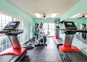 Thumbnail 11 of 23 - A gym with treadmills, elliptical machines, and a fan.