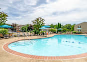 Thumbnail 5 of 23 - A large outdoor swimming pool surrounded by trees and umbrellas.