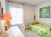 Thumbnail 20 of 23 - A bedroom with a bed, a table, a chair, a lamp, and a painting on the wall.