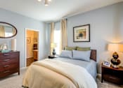 Thumbnail 21 of 23 - A bedroom with a large bed, a dresser, and a nightstand with a lamp.