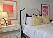 Thumbnail 32 of 36 - A white bed with a white headboard and a white nightstand with a lamp and a picture frame on it.