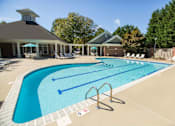 Thumbnail 1 of 28 - A swimming pool with a diving board and a building in the background.