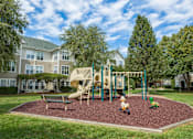 Thumbnail 22 of 28 - A playground with a slide, swings, and a seesaw in the foreground with apartment buildings in the background.