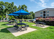 Thumbnail 37 of 40 - A blue umbrella is over a picnic table in a grassy area.