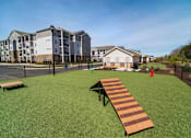 Thumbnail 54 of 64 - A long wooden bench sits on a green lawn in front of apartment buildings.