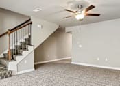 Thumbnail 9 of 23 - 3-Bedroom Townhomes in Belton, MO - Traditions Townhomes - A Spacious Empty Room with Carpet Flooring, Ceiling Fan with Light, and a Carpeted Staircase.