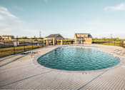 Thumbnail 3 of 23 - Pet-Friendly Townhomes in Belton, MO - Traditions Townhomes - An Outdoor Swimming Pool Surrounded by a Deck, Blank Fence, and Landscaping, Overlooking a Pavilion and the Clubhouse.