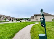 Thumbnail 20 of 23 - A green signpost stands in a grassy area with a path leading to a residential area.