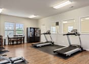 Thumbnail 14 of 28 - A room with a treadmill, a refrigerator, and a dining table.