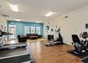 Thumbnail 15 of 28 - Lawrence, KS, Apartments Near Lawrence Rotary Arboretum - Remington Square - Fitness Center with Wood Flooring, Treadmills, Table, Chairs, Vending Machines, Light Fixtures, and Glass Windows.