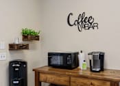 Thumbnail 17 of 28 - A coffee bar with a coffee maker, microwave, and a coffee pot on a wooden table.