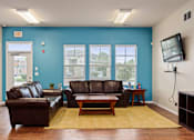 Thumbnail 18 of 28 - Lawrence, KS, Apartments Near University of Kansas - Remington Square - Resident Lounge with Wood Flooring, Two Brown Leather Couches, Coffee Table, Side Tables, Mounted TV, and Light Fixtures.
