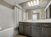 Thumbnail 41 of 41 - A bathroom with a white tub, sink, and grey cabinets.