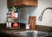 Thumbnail 7 of 28 - A kitchen counter with a sink, a plant, and a sign that says "Feels good to be home".