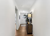 Thumbnail 2 of 26 - a hallway with white walls and a wooden floor and a table with a lamp