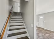 Thumbnail 6 of 15 - A staircase with wooden handrails and grey steps leads to a white door.