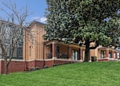 Thumbnail 2 of 13 - A large building with a red brick wall and a green lawn in front.