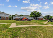 Thumbnail 16 of 19 - A playground with a slide and a tree in the middle of a grassy area.