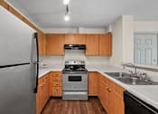 Thumbnail 14 of 25 - A kitchen with a stainless steel refrigerator, a stove, and wooden cabinets.
