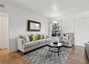 Thumbnail 4 of 19 - A living room with a white couch, a coffee table, and a chair with a patterned cushion.
