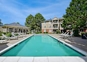 Thumbnail 11 of 25 - A swimming pool in front of a building with a fence and trees in the background.