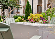 Thumbnail 146 of 149 - A white bench is in front of a white wall with a tree and flowers in the background.