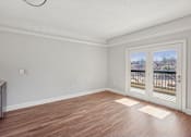 Thumbnail 7 of 27 - A room with wooden flooring and a view of a balcony through the sliding glass door.