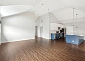 Thumbnail 6 of 13 - A spacious room with wooden floors and a kitchen area with white cabinets.