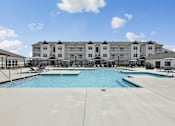 Thumbnail 3 of 26 - A large swimming pool in front of a multi-story apartment building.