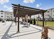 Thumbnail 5 of 26 - A pool sundeck with a table and chairs under a wooden pergola.