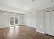 Thumbnail 9 of 27 - A room with wooden floors and white walls, with a door on the right side.