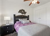 Thumbnail 8 of 19 - A bedroom with a bed, nightstand, and ceiling fan.