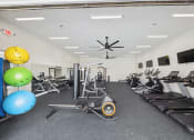 Thumbnail 31 of 36 - a gym with cardio machines and weights and a ceiling fan