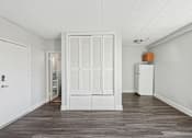 Thumbnail 9 of 13 - A room with white walls and a wooden floor with a white door and a white cabinet with a box on top of it.
