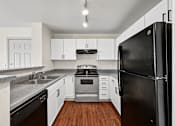 Thumbnail 2 of 25 - A black refrigerator stands in a kitchen with white cabinets and a stove.