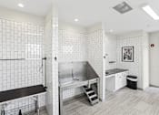 Thumbnail 33 of 36 - A white tiled bathroom with a sink, mirror, and a bench.