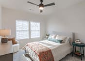 Thumbnail 10 of 29 - A bedroom with a bed, a ceiling fan, and a small table with a plant on it.