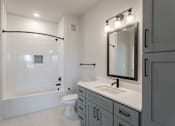 Thumbnail 12 of 29 - A modern bathroom with a white tub, sink, and grey cabinets.