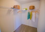 Thumbnail 53 of 65 - A white closet with clothes hanging and baskets on the shelf.