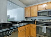 Thumbnail 25 of 41 - A kitchen with wooden cabinets and black countertops.