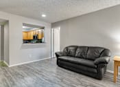 Thumbnail 29 of 41 - A black leather couch sits in a living room with a wooden table and a painting on the wall.