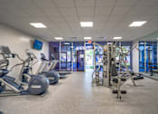 Thumbnail 14 of 24 - a gym with cardio equipment and weights in a building with glass doors