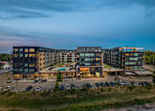 Thumbnail 53 of 54 - A large, modern building complex with a parking lot in front.