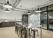 Thumbnail 17 of 26 - A kitchen with a table and stools in the foreground and a glass wall in the background.
