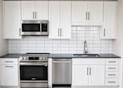 Thumbnail 4 of 17 - Modern kitchen with white cabinets and stainless steel appliances at The Avery - Residential Apartments, Fargo, North Dakota