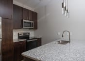 Thumbnail 11 of 37 - a kitchen with granite countertops and dark wood cabinets  at RoCo Apartments, Fargo, North Dakota 58102