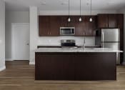 Thumbnail 28 of 37 - a kitchen with a large island with granite countertops and dark wood cabinets  at RoCo Apartments, Fargo, North Dakota, 58102