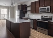Thumbnail 10 of 37 - a kitchen with dark wood cabinets and an island with a granite countertop and stainless steel appliances  at RoCo Apartments, Fargo, ND 58102
