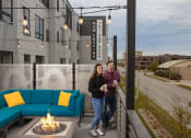 Thumbnail 76 of 84 - a man and a woman standing on a patio with a fire pit and a blue couch at The Landing at 1001 NP, Fargo, ND, 58102