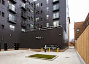 Thumbnail 10 of 29 - A courtyard with a bench and grass patch in front of a black building  at Mercantile on Broadway, Fargo, North Dakota 58102